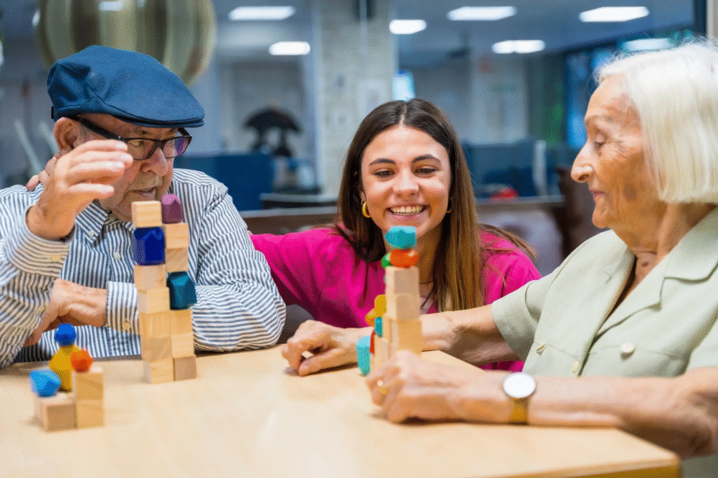A young caretaker smiles as she assists a senior man and woman play a game at an adult day program.